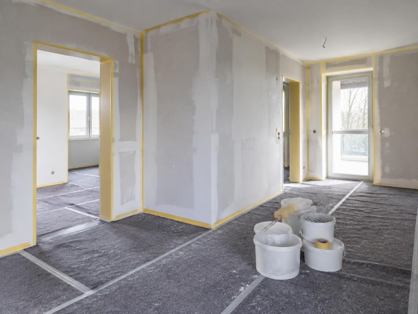 Frisch gespachtelte Wand mit Farbrolle und Eimer im leeren Raum